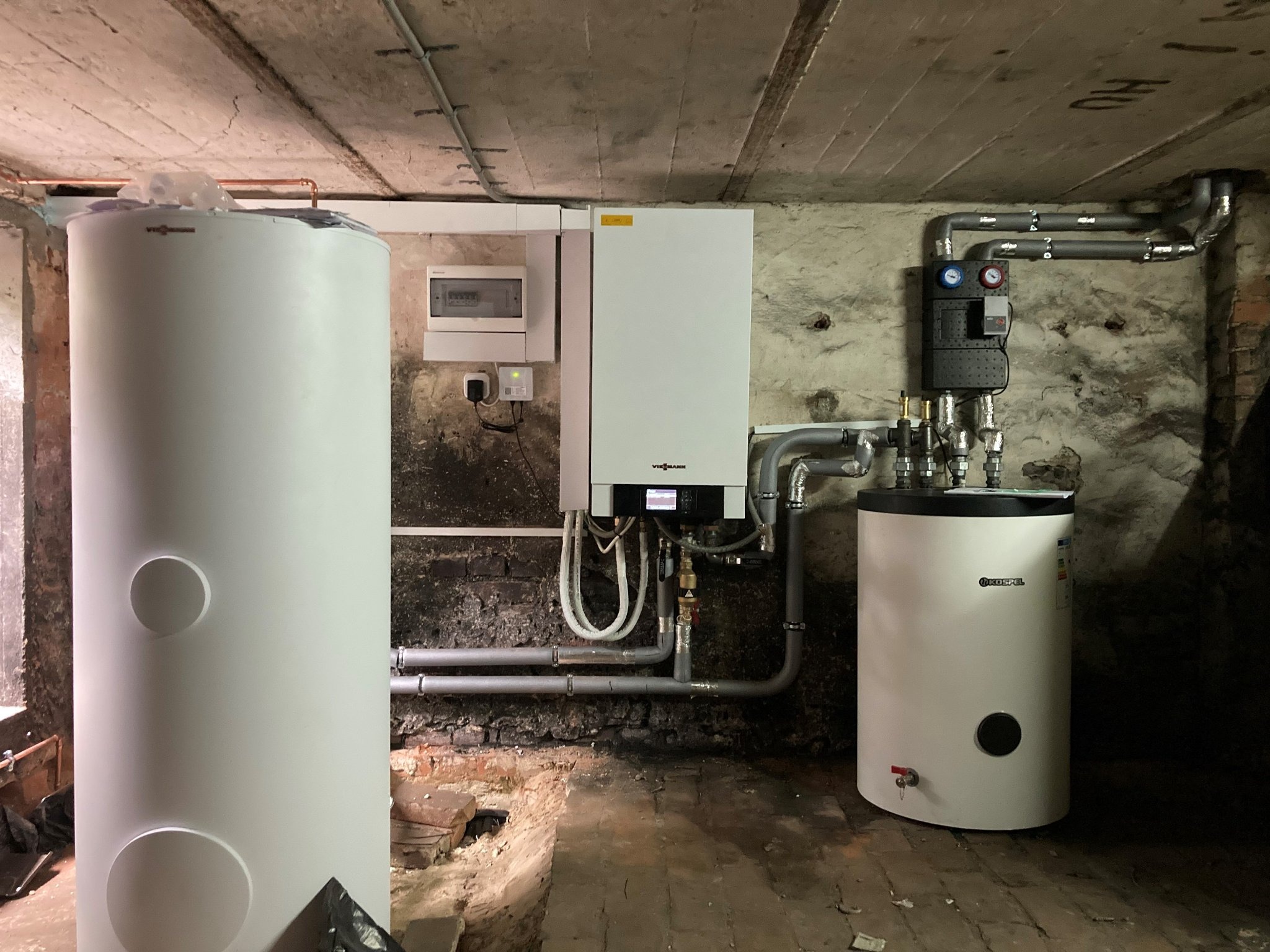 Instalacja kotła grzewczego Viessmann z dwoma zasobnikami ciepłej wody w piwnicy o surowych ścianach z cegły i betonu.