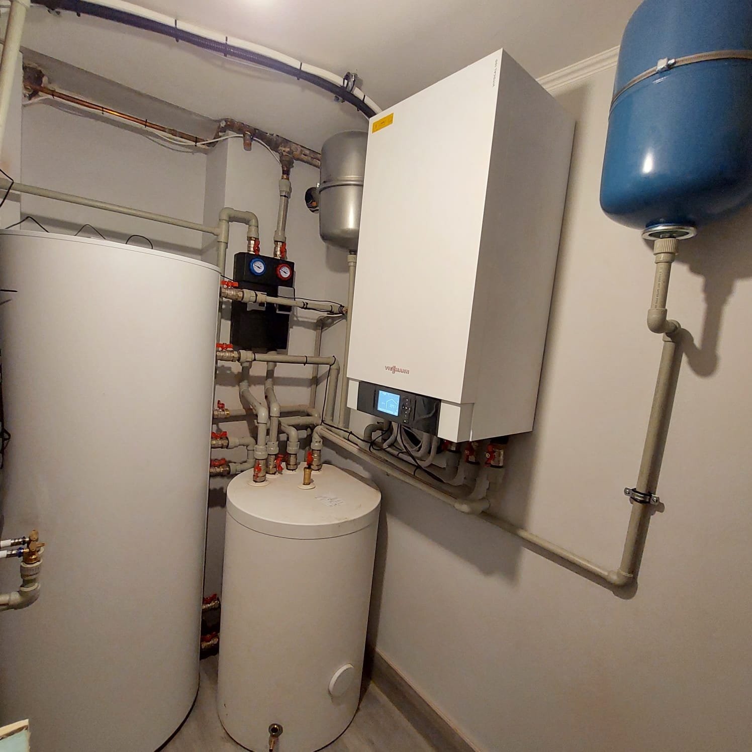 Instalacja kotłowni z białym kotłem Viessmann, zbiornikami akumulacyjnymi i niebieskim naczyniem przeponowym, widoczne liczne rury i zawory.