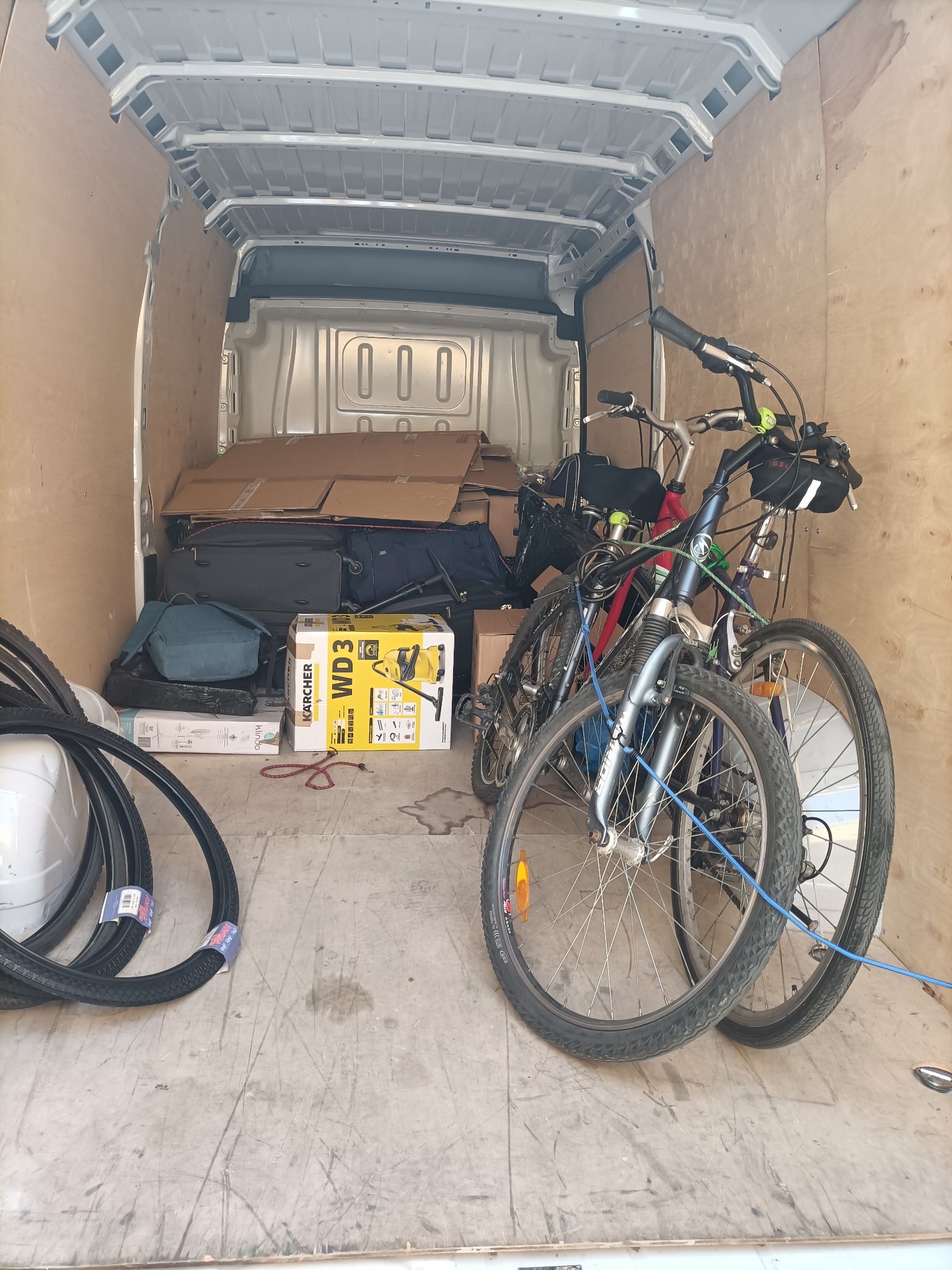 Wnętrze furgonetki z zabezpieczonymi rowerami, kartonami, walizkami i odkurzaczem Kärcher WD 3 podczas transportu.