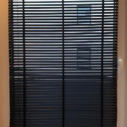 Ciemne poziome listwy w oknie, częściowo zasłonięte, widoczne linki sterujące po lewej stronie, okno z białą ramą i klamką.