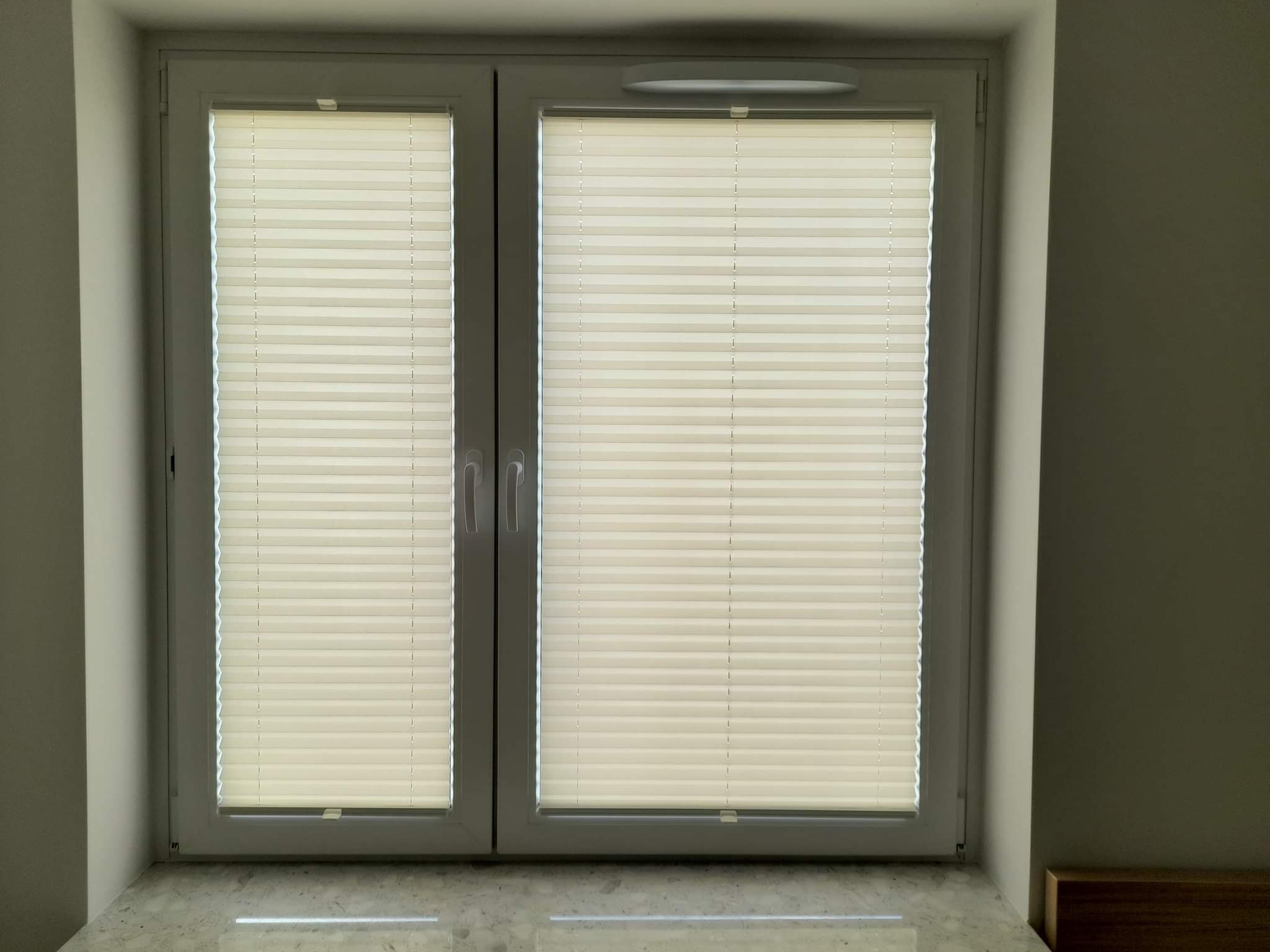 Okna PCV z zamontowanymi jasnymi plisowanymi osłonami okiennymi, widok z bliska, marmurowy parapet.