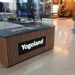 Wyspa handlowa Yogoland z drewnianą okładziną i czarnym blatem w galerii handlowej, z dystrybutorami i pojemnikami na składniki.