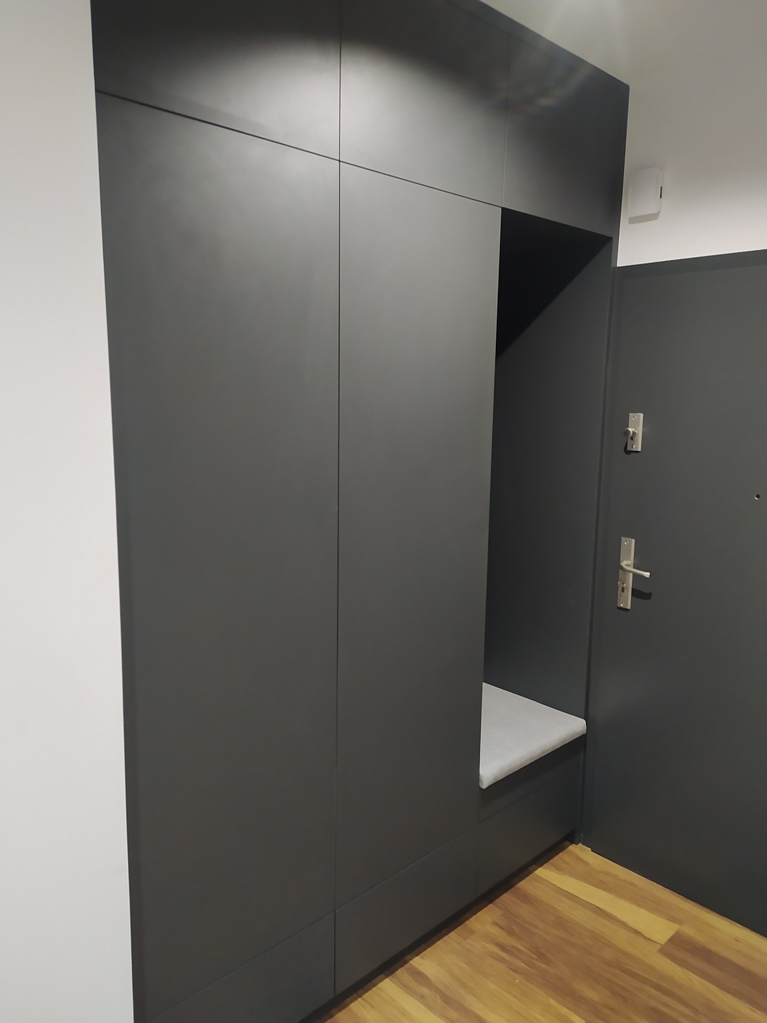 Grafitowa szafa wnękowa z siedziskiem w przedpokoju, minimalistyczny design, drewniana podłoga.
