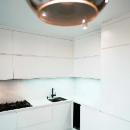 Minimalistyczna, biała kuchnia z marmurowym blatem i podłogą, czarna armatura, oświetlenie LED pod szafkami, nowoczesna lampa wisząca w kadrze.