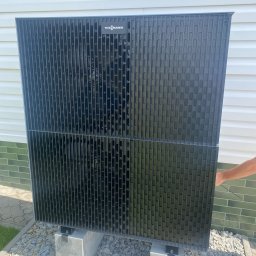 Alpineclima Michał Zagrabski - Czarna pompa ciepła marki Viessmann zamontowana na betonowych podstawach, widoczna część elewacji budynku w tle.