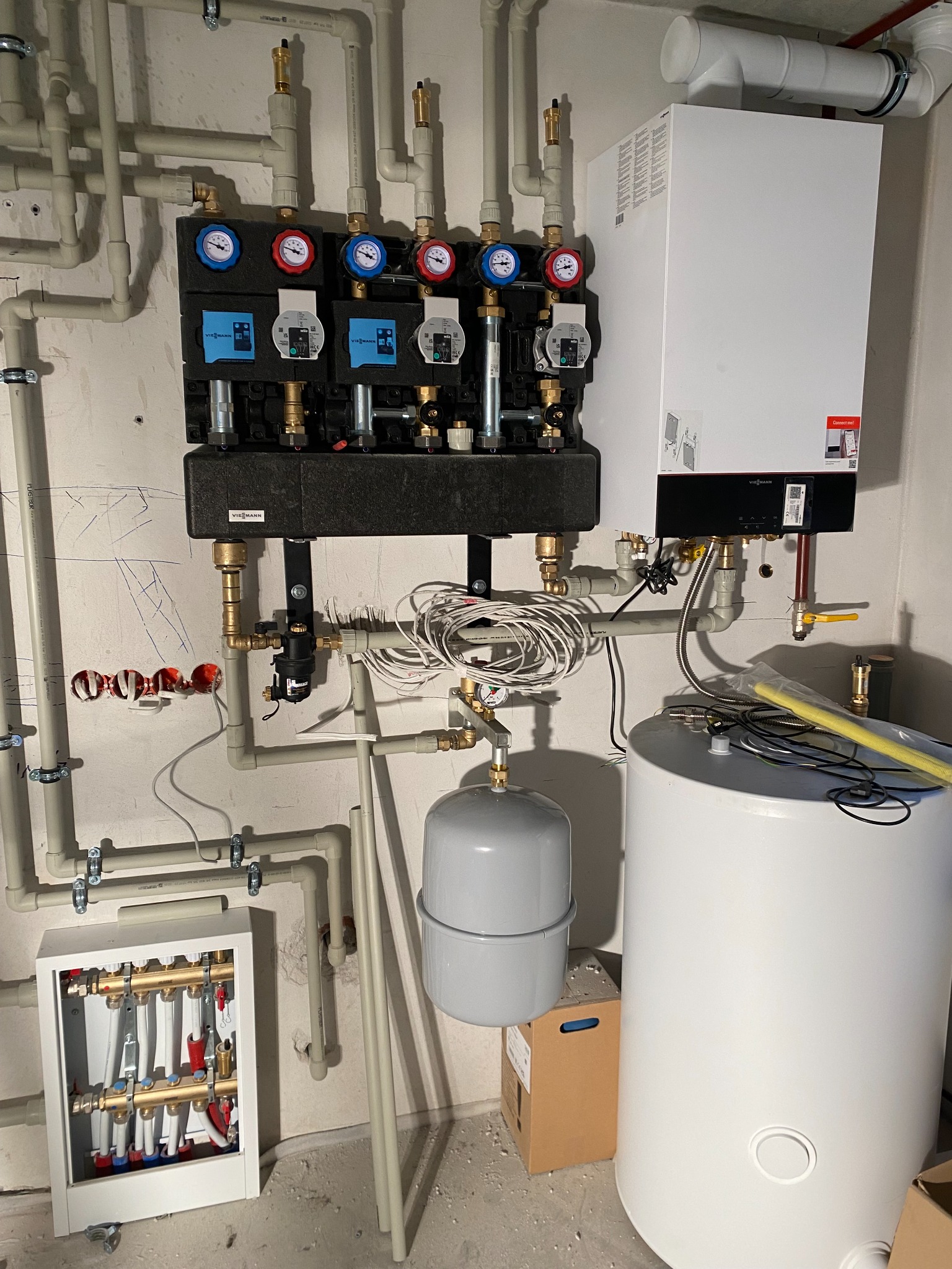 Instalacja grzewcza w kotłowni: biały piec gazowy Viessmann, rozdzielacz z manometrami, zbiornik wyrównawczy, instalacja rur z tworzywa sztucznego, skrzynka rozdzielcza z zaworami.
