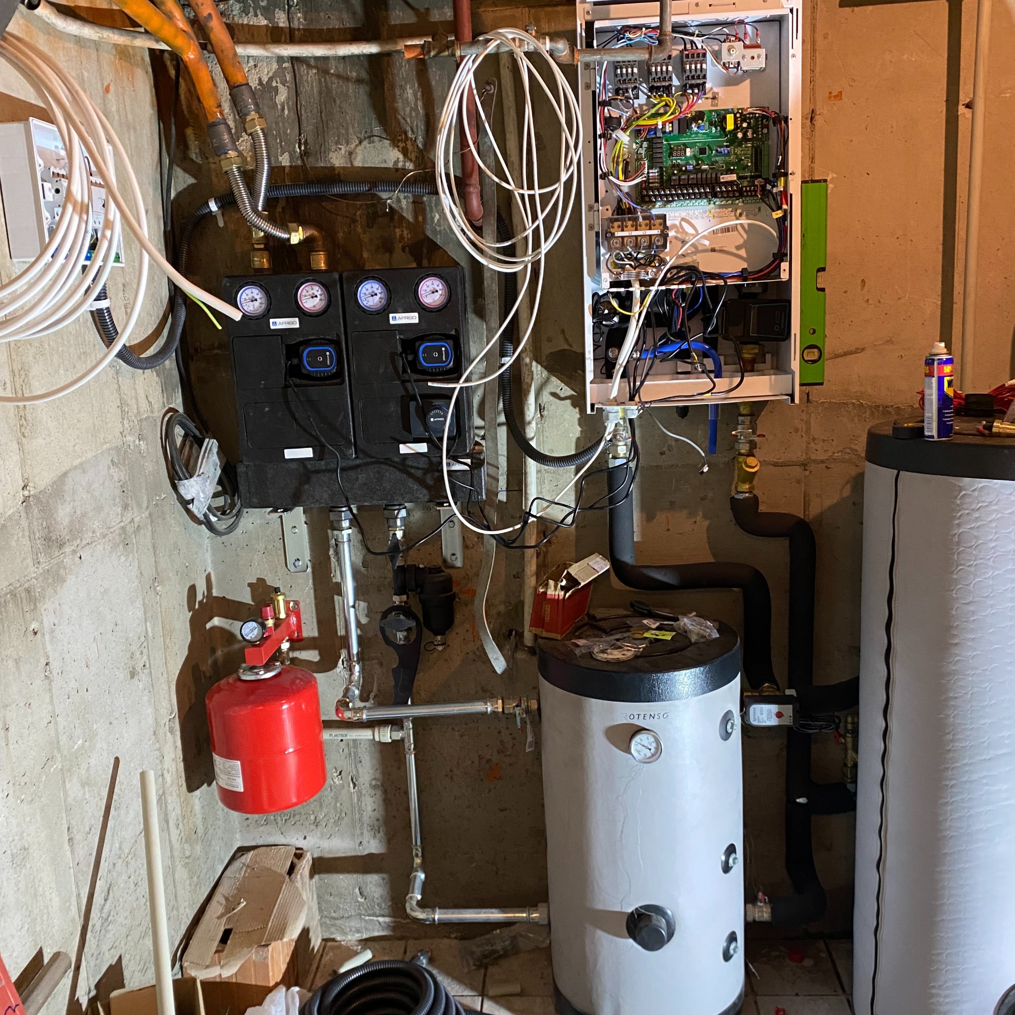 Instalacja kotła gazowego w piwnicy z widocznymi elementami: zbiornik buforowy, manometry, automatyka i instalacja elektryczna, w tle surowe ściany piwniczne.