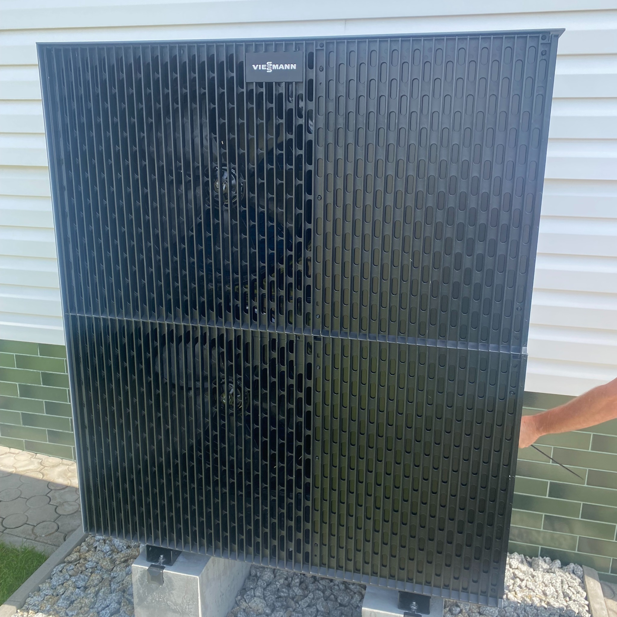 Czarna pompa ciepła marki Viessmann zamontowana na betonowych podstawach, widoczna część elewacji budynku w tle.