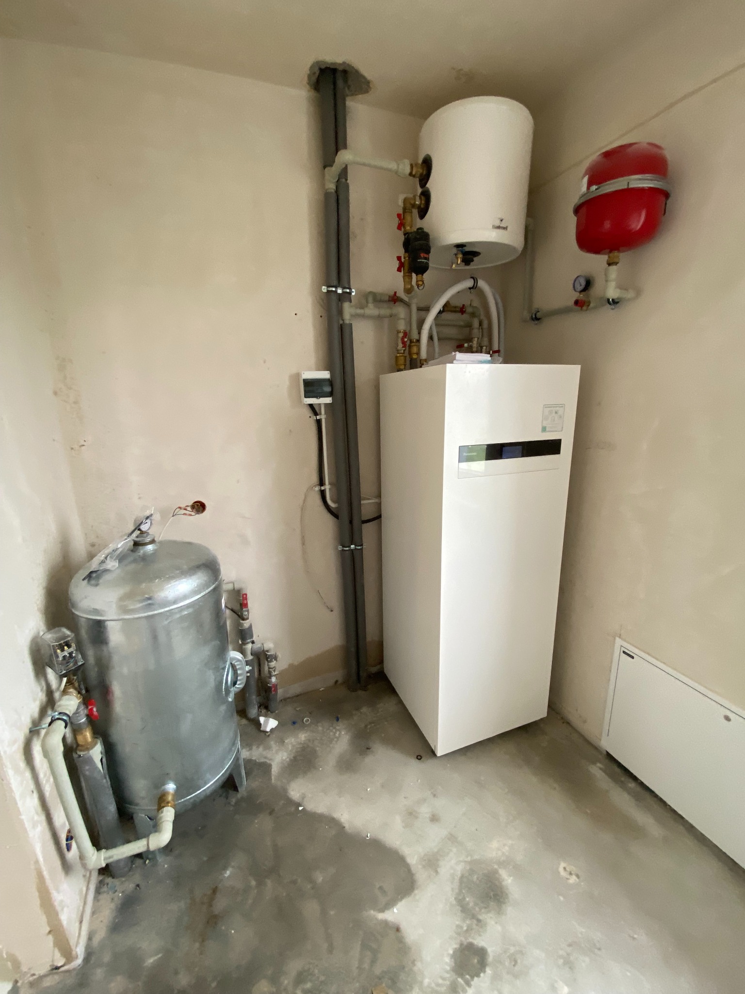 Biała jednostka centralna z zbiornikami wyrównawczymi w kotłowni z surowymi ścianami i betonową podłogą ze śladami wilgoci