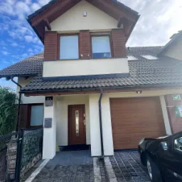 Dom jednorodzinny z zamontowanymi kamerami monitoringu na elewacji pod oknami na pierwszym piętrze, widoczne również elementy systemu alarmowego na ścianie.