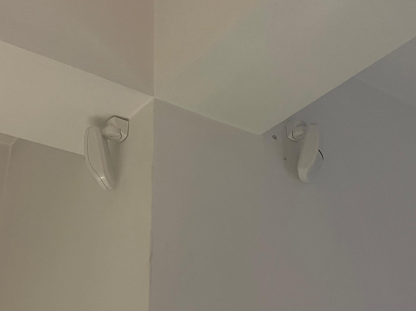 Zamontowane czujki alarmowe z uchwytami w rogu pomieszczenia, widoczne śruby mocujące.