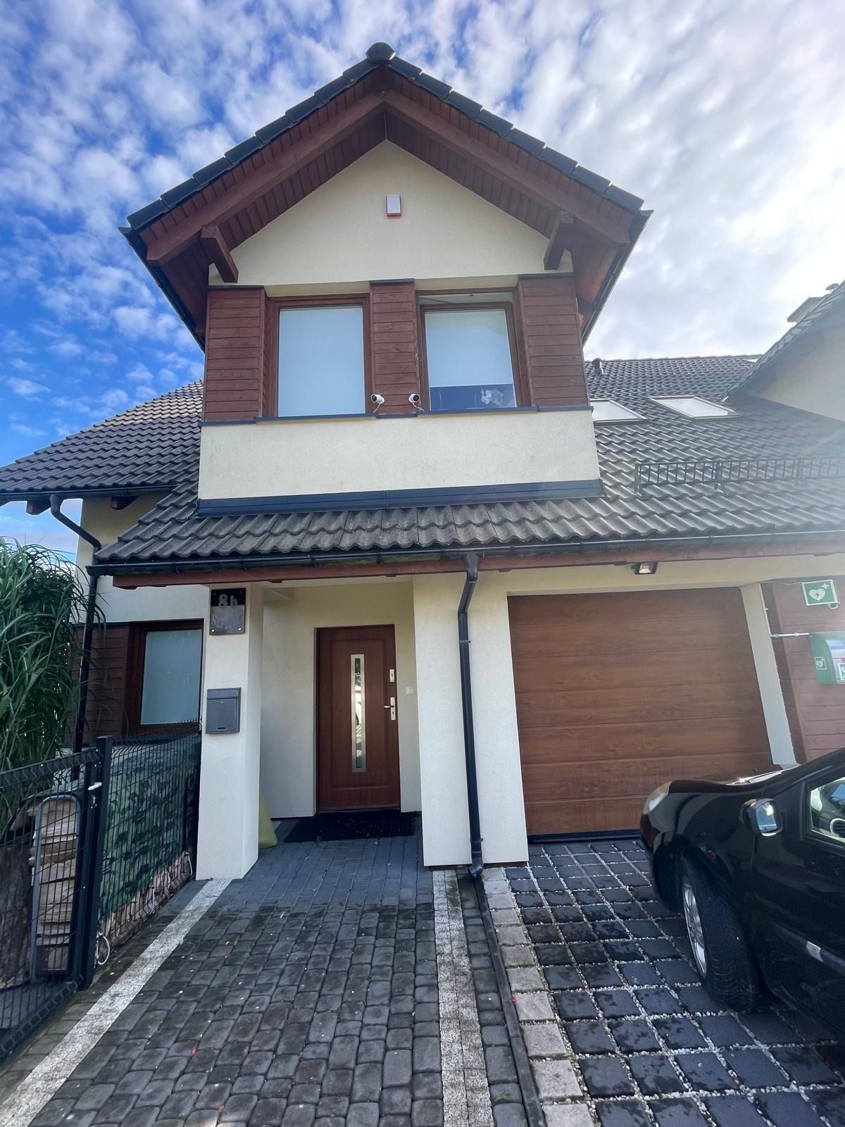 Dom jednorodzinny z zamontowanymi kamerami monitoringu na elewacji pod oknami na pierwszym piętrze, widoczne również elementy systemu alarmowego na ścianie.