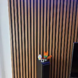 Ściana z drewnianych paneli pionowych z podświetleniem LED na górze, obok kolumny głośnikowej z dekoracjami, na podłodze drewniany parkiet.