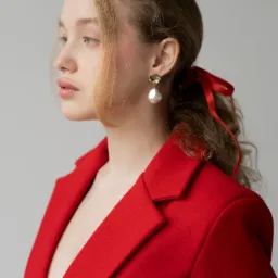 Profil młodej kobiety w czerwonej marynarce, z upiętymi włosami ozdobionymi czerwoną wstążką i perłowym kolczykiem