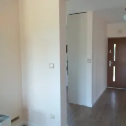 Pomieszczenie po odświeżeniu koloru ścian na delikatny odcień różu, widoczne drewnopodobne panele podłogowe, białe listwy przypodłogowe i framuga drzwi.