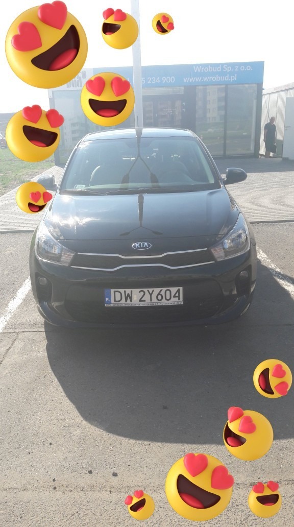 Czarny samochód marki Kia z polską tablicą rejestracyjną DW 2Y604, udekorowany emotikonami z sercami zamiast oczu, zaparkowany przed budynkiem firmy Wrobud Sp. z o.o.