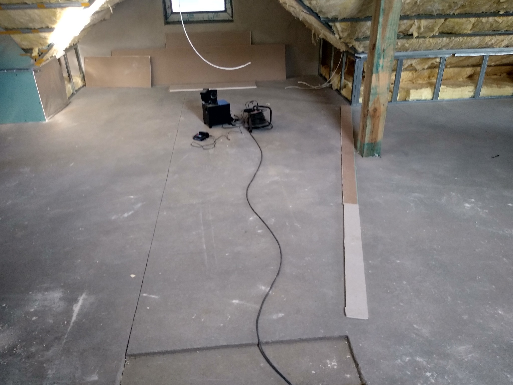 Poddasze w trakcie ocieplania, widoczne wełna mineralna między metalowymi profilami, płyty OSB i karton gips, sprzęt budowlany i głośniki na posadzce