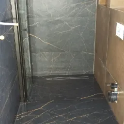 Nowoczesna kabina prysznicowa z czarnymi płytkami imitującymi marmur ze złotymi żyłami oraz odpływem liniowym w podłodze.