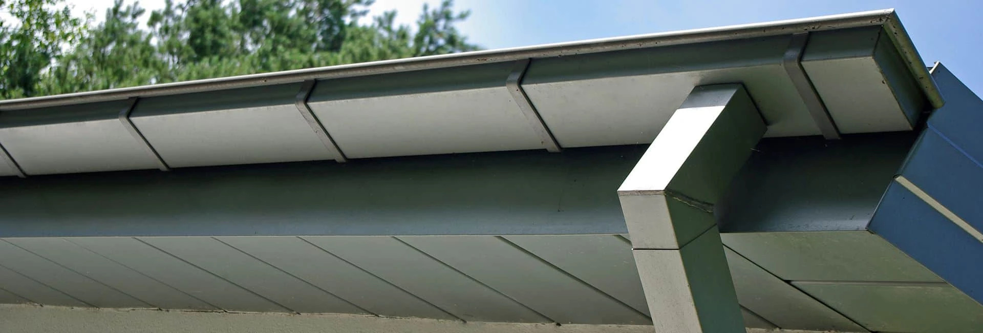 Szare podbitka dachowa i rynna z metalu, widoczne mocowania i fragment elewacji budynku.