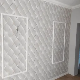 Ściana wykończona panelami 3D w romby, z ukrytymi drzwiczkami rewizyjnymi w białych ramkach, widoczne przewody elektryczne w jednej z nich.