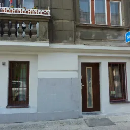 Fasada budynku z szyldem 'Serwis TV', okna z kratami i balkon z balustradą.