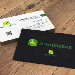 Stos wizytówek, w tym czarna wizytówka John Deere i biała wizytówka Agro-Efekt, leżą na drewnianym stole pod kątem, prezentując logo i dane kontaktowe.