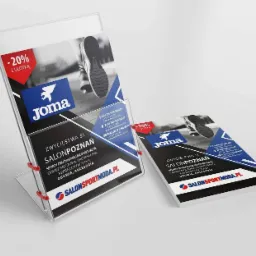 Dwie ulotki reklamowe marki Joma, jedna umieszczona w przezroczystym stojaku z czerwonymi elementami, druga leżąca obok. Ulotki prezentują ofertę sklepu sportowego Salon Poznań z odzieżą, obuwiem...