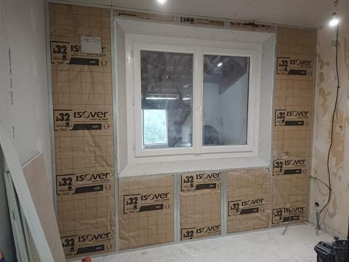 Ściana z oknem w trakcie ocieplania, widoczne płyty izolacyjne Isover, surowy stan wykończenia, przygotowanie do dalszych prac.