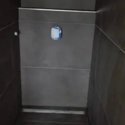 Wnętrze kabiny prysznicowej w Kaszowie, wykończonej ciemnymi płytkami ceramicznymi z metalowymi listwami dekoracyjnymi. Na podłodze widoczne ślady butów.