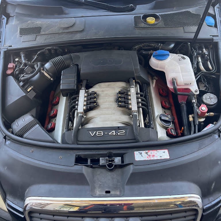 Silnik V8 4.2 litra w komorze silnikowej samochodu Audi, widoczne elementy układu chłodzenia, wtryskiwacze i osprzęt, lekko zakurzone elementy.