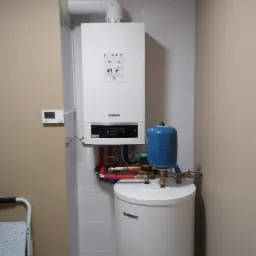 Biały piec gazowy marki Buderus z niebieskim zbiornikiem wyrównawczym, zamontowany na białej ścianie z płytek, widoczny regulator temperatury na sąsiedniej ścianie.