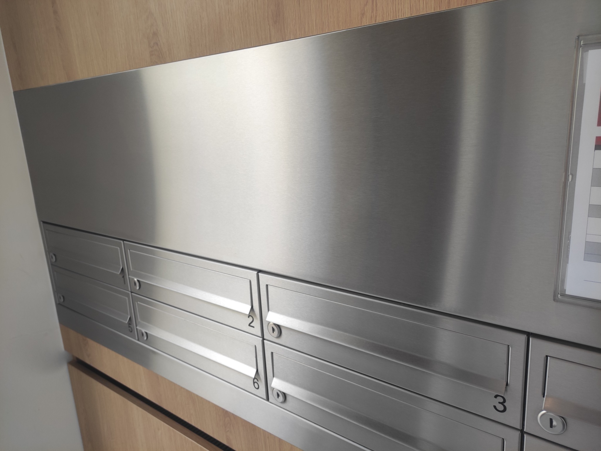 Metalowe skrzynki pocztowe w budynku biurowym w Warszawie, zamontowane na drewnianej ścianie.