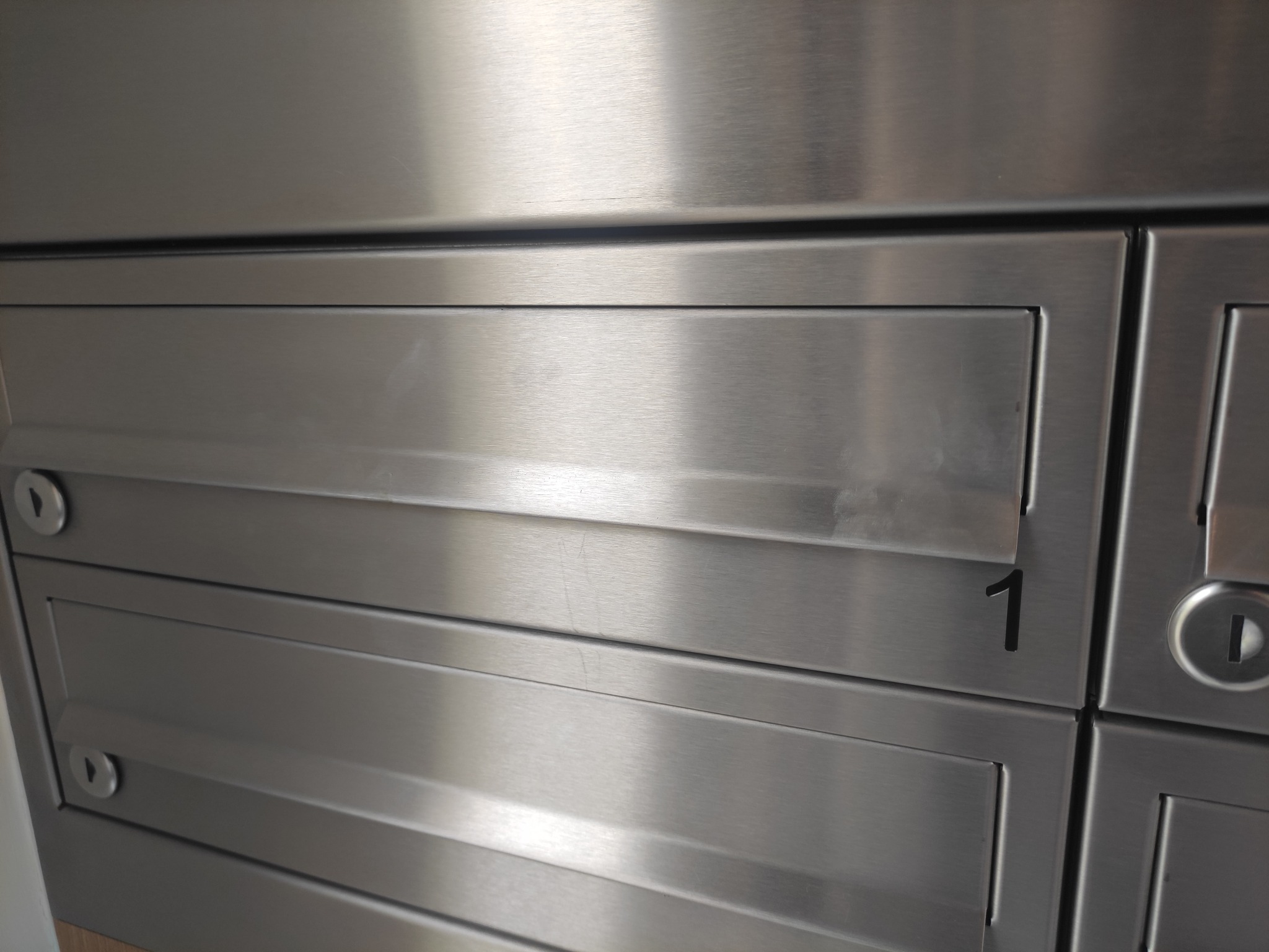 Szczegółowy widok metalowych skrzynek pocztowych wewnątrz budynku, skrzynka numer 1 z zamkiem na klucz.