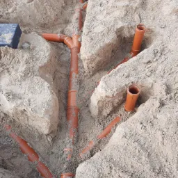 Wykonane w wykopie połączenia rur kanalizacyjnych z tworzywa sztucznego, częściowo zasypane piaskiem.
