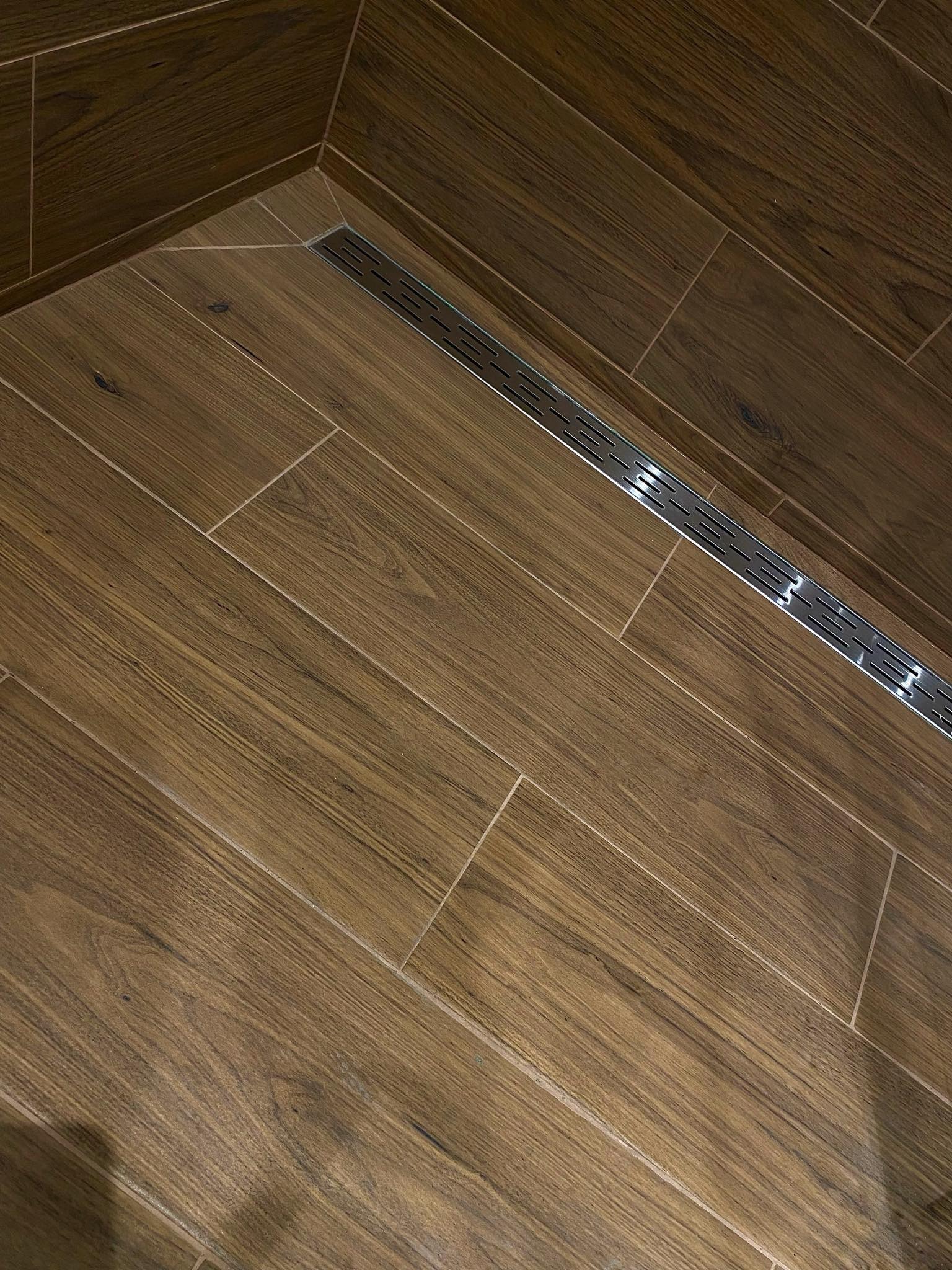 Ukośne ułożenie płytek imitujących drewno w łazience, z widocznym liniowym odpływem prysznicowym ze stali nierdzewnej.