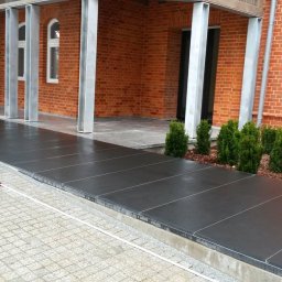 Kamieniarstwo.pl - Nowoczesny taras z ciemnych płyt kamiennych, z widoczną kostką brukową i ceglaną elewacją budynku w tle.