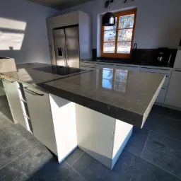 Nowoczesna kuchnia z wyspą i blatem z ciemnego kamienia, widok na okno z zimowym krajobrazem, minimalistyczny design.