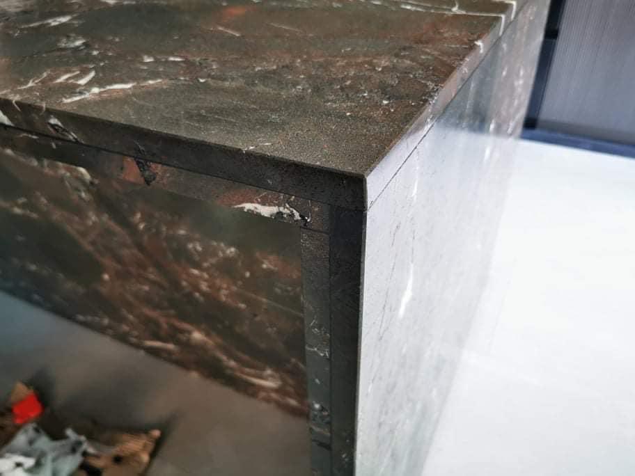 Fragment blatu z ciemnego kamienia z białymi żyłkami, widoczny narożnik i krawędź, nałożony na jasną powierzchnię.