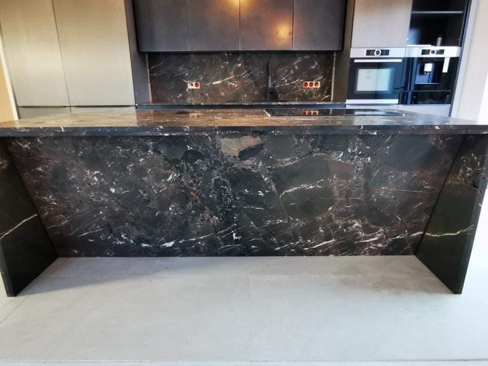 Czarny, polerowany blat kuchenny z kamienia naturalnego z wyraźnym białym żyłkowaniem, dopasowany do ściany nad blatem i nowoczesnej zabudowy kuchennej w tle.