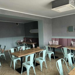 Kacper Skorb Usługi Budowlane - Wnętrze lokalu po malowaniu: pastelowe ściany, drewniane stoły i miętowe krzesła. Dekoracyjne detale, w tym lustra i tekstylia, dopełniają nowoczesny, minimalistyczny styl.