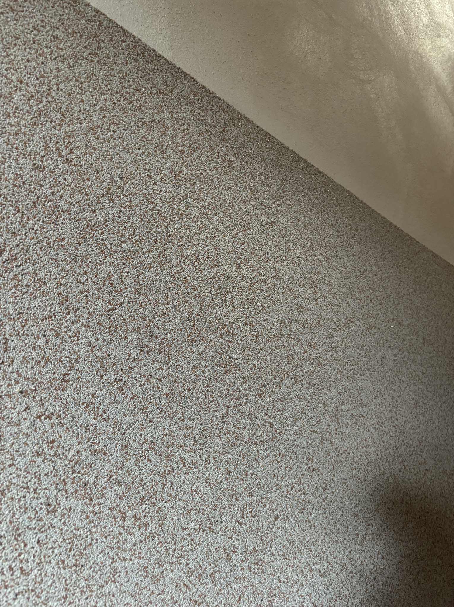 Ściana pokryta dekoracyjnym tynkiem strukturalnym w odcieniach beżu i brązu, widoczna z bliska, z fragmentem sufitu w górnym rogu.