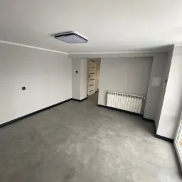 Nowoczesne, puste wnętrze z szarymi ścianami, płytkami podłogowymi imitującymi beton, białym grzejnikiem i minimalistycznym oświetleniem sufitowym.