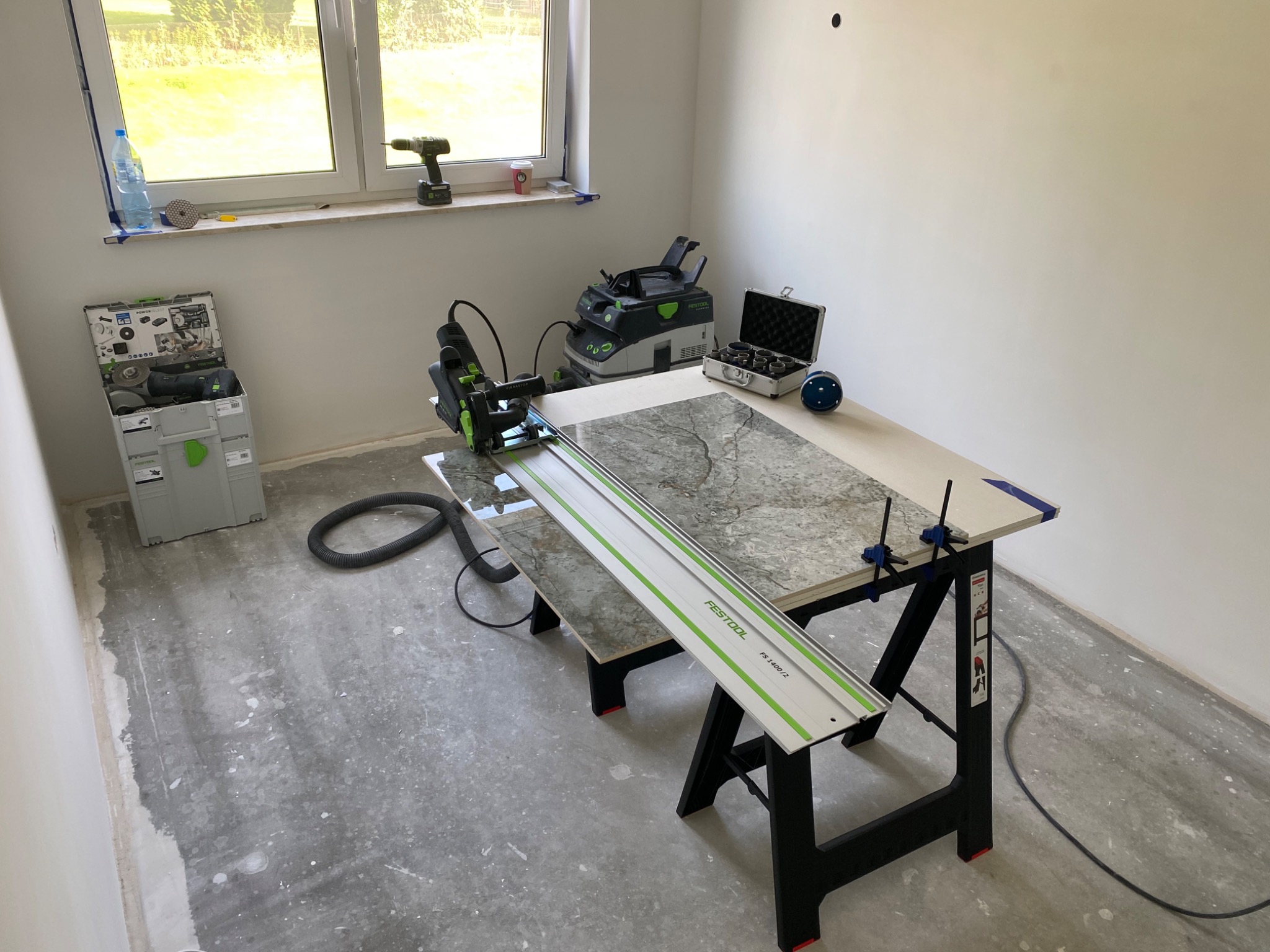 Przygotowanie do cięcia płytek marmurowych na stole warsztatowym Festool z użyciem pilarki zagłębiarki, odkurzacza przemysłowego i szyny prowadzącej; widoczne narzędzia i akcesoria do obróbki...