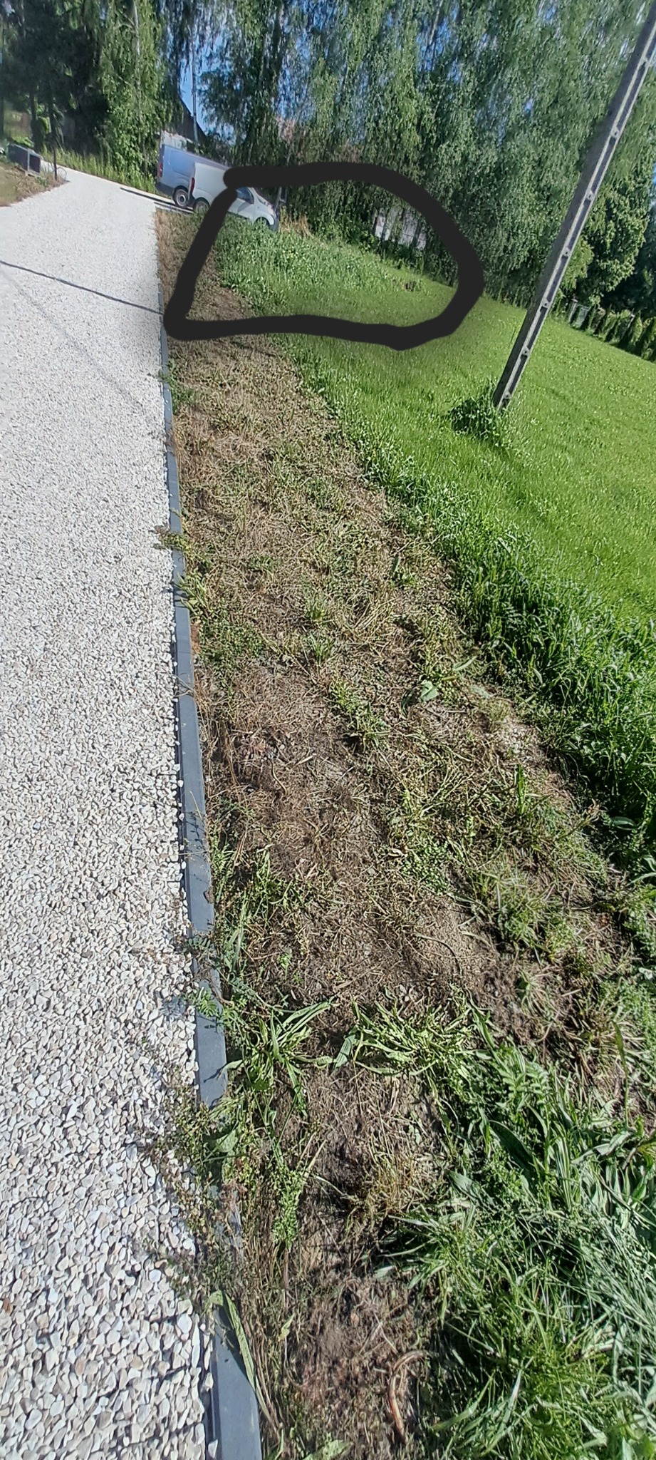 Fragment ogrodu po niwelacji terenu, widoczna granica między utwardzoną drogą z kamienia a przygotowanym podłożem pod trawnik. W tle zaparkowany bus.