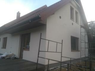 Elewacja domu jednorodzinnego po nałożeniu jasnego tynku, widoczne rusztowanie i fragment dachu z kominem.