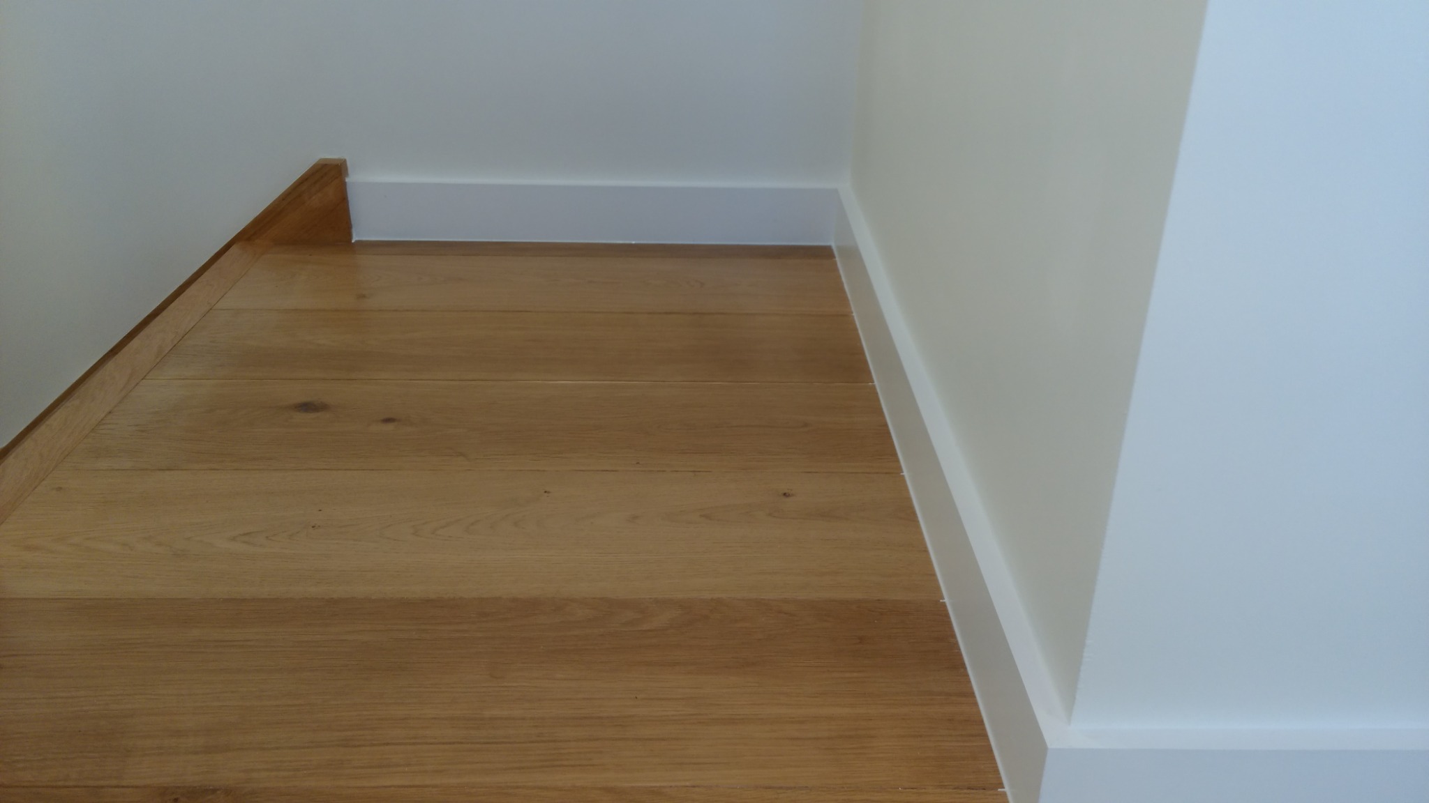 Parkiet dębowy ułożony przy białej listwie przypodłogowej i drewnianej listwie schodowej, widok z góry.