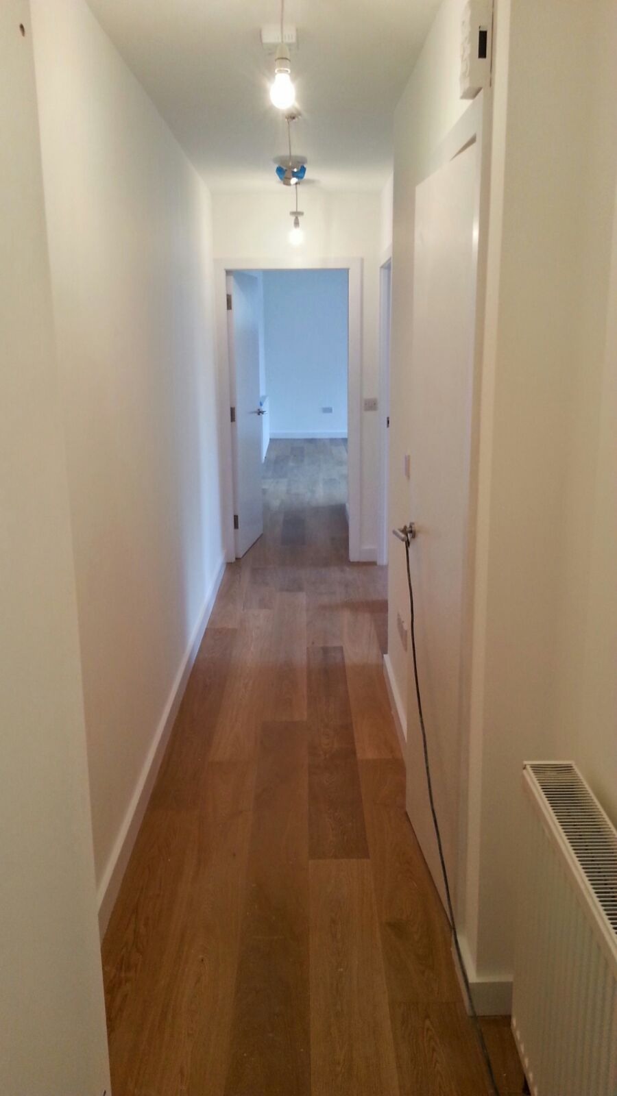 Wnętrze korytarza po remoncie w London: świeżo pomalowane białe ściany, drewniana podłoga, widoczne drzwi i grzejnik.