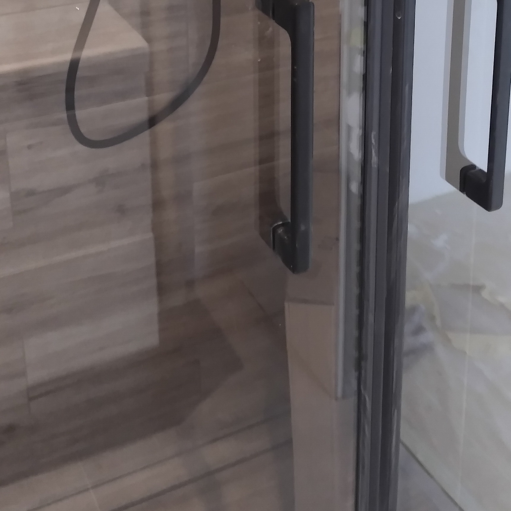 Szczegółowe ujęcie kabiny prysznicowej z ciemnymi uchwytami i płytkami imitującymi drewno wewnątrz.