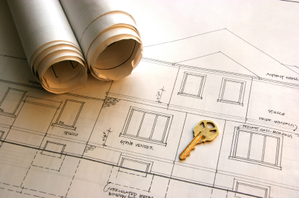 Architektoniczny plan domu z dwoma zwiniętymi rysunkami technicznymi i złotym kluczem na wierzchu, ukazujący detale elewacji i okien.