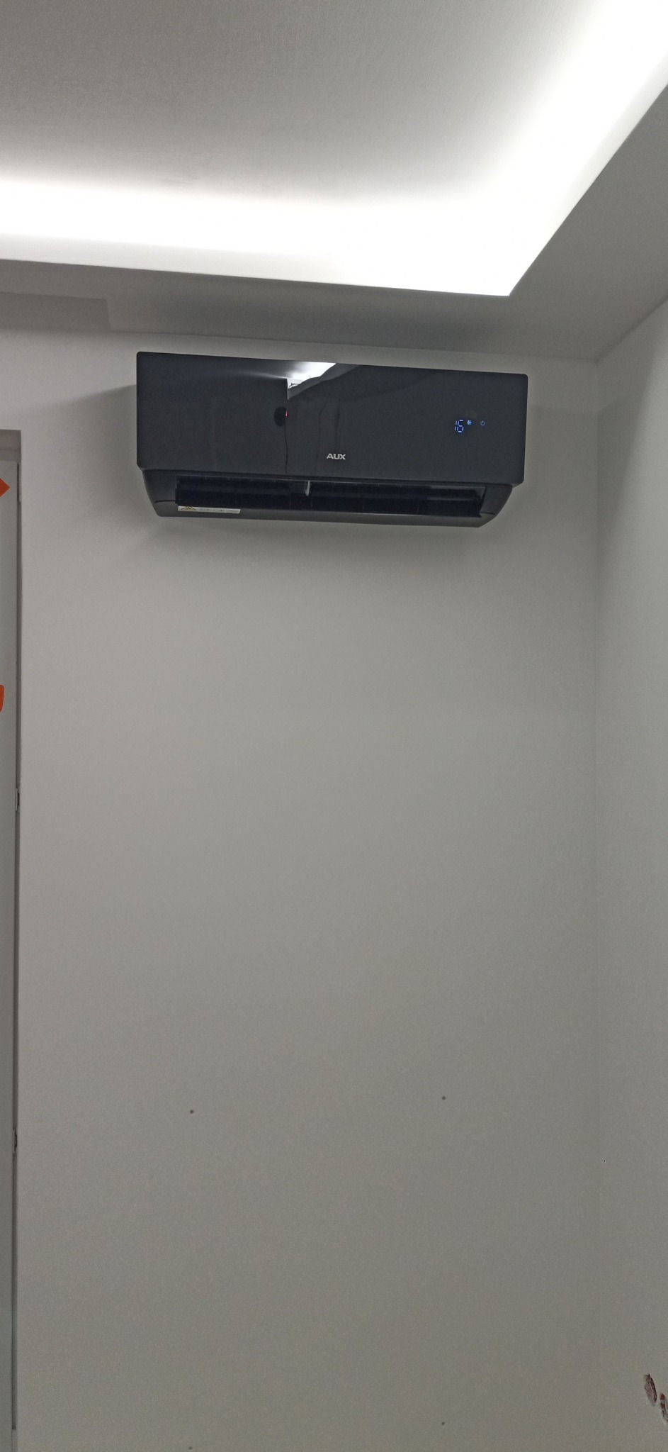 Czarny klimatyzator AUX zamontowany na szarej ścianie w pomieszczeniu z oświetleniem LED na suficie, wyświetlający temperaturę 16 stopni Celsjusza.